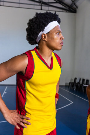 African American male athlete standing hands on hips on basketball court wearing yellow red jersey....
