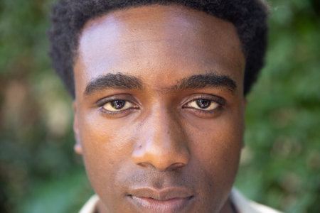 African American man posing for portrait shoot in park wearing collared shirt with foliage backdrop....