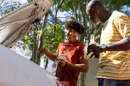 Diverse male friends inspecting engine oil under open car hood in driveway. Automotive, friendship,...
