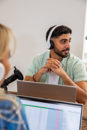 Diverse coworkers recording audio with microphone and silver laptop in modern studio. Studio, podcast, collaboration, technology, recording, creative, professionalの写真素材