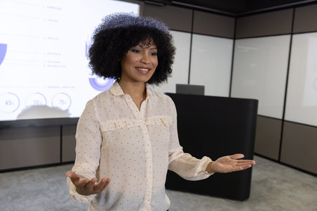 Mid-adult African American woman standing presenting data on screen with podium in conference room....