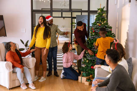 African American family decorating Christmas tree in living room at home with ornaments gifts. Festive, celebration, tradition, warmth, togetherness, joy, cozyの写真素材