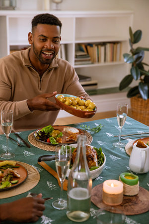African American man serving ceramic bowl of baby potatoes at home dining table, copy space. Family gathering, comfort, rustic, lifestyle, home interior, conviviality, wellbeingの写真素材