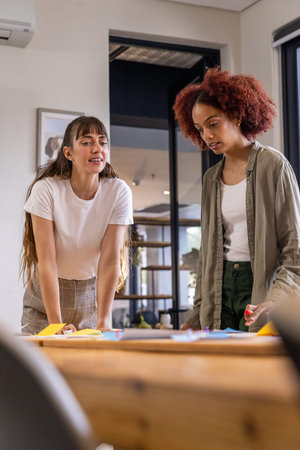 Diverse female colleagues brainstorming over wooden table at office with sticky notes, markers. Collaboration, innovation, teamwork, creative workspace, modern design, business strategyの写真素材