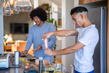 Diverse male friends preparing breakfast at kitchen island with grinder, toaster, copy space. Contemporary, casual, vibrant, social, culinary, homey, freshの写真素材