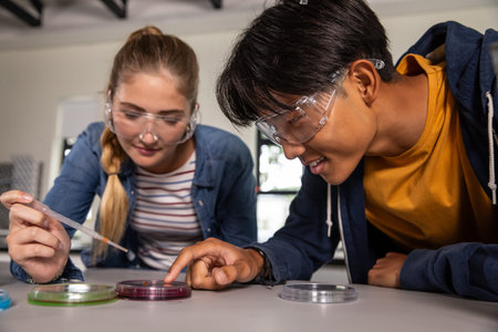 Female student and Asian teenage male student using pipette at petri dishes in lab wearing goggles. Science, education, experimentation, research, discovery, collaboration, innovationの写真素材