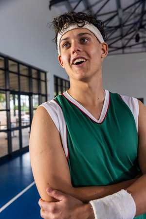 Teenage male standing on basketball court at gym wearing green jersey, white headband and wristband. Athlete, sports, activity, athletic, teamwork, fitness, energeticの写真素材