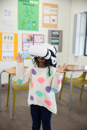 African American school-age girl standing in classroom wearing VR headset and exploring VR world....
