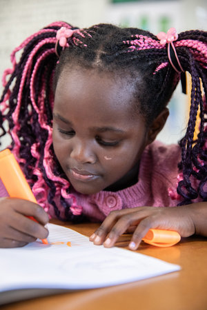 African American child leaning forward at study desk highlighting notes with orange highlighter....