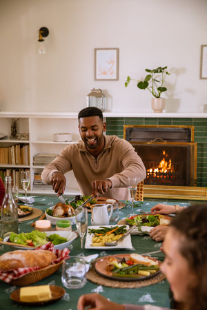 Diverse friends carving roast poultry at dining table with salad bowls bread basket wine glasses....