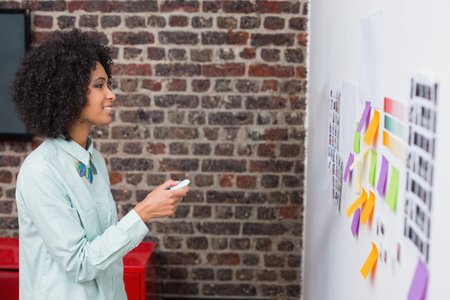 African American woman holding presenter, standing at office with mint green shirt and sticky notes....