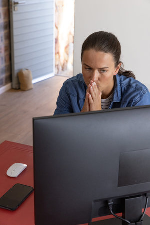 Woman sitting at home office desk wearing denim shirt focusing on monitor with mouse smartphone....