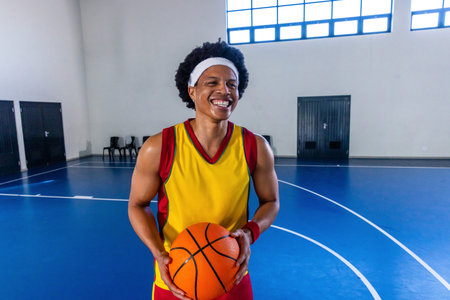 African American man dribbling basketball on blue court wearing yellow red jersey and shorts....