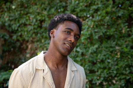 African American man standing and gazing upward to right in garden with ivy backdrop. Nature,...
