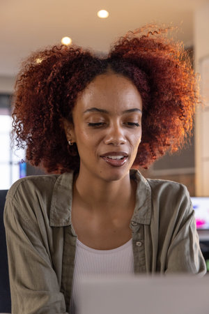 African American woman typing on laptop in home office with monitors and warm overhead lights....