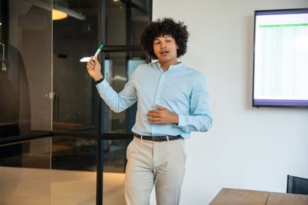 African American man in 30s holding green marker and presenting spreadsheet in conference room....