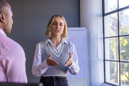 Diverse coworkers wearing office attire presenting on flipchart and listening by window at office. Professional, collaboration, communication, brainstorming, meeting, urban, modernの写真素材