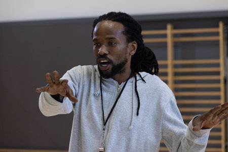 Mature African American male coach standing in gym with whistle on lanyard gesturing palms downward. Training, fitness, athletic, motivation, determination, discipline, functionalの写真素材