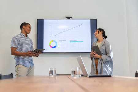 Diverse colleagues presenting charts on tablets and wall-mounted display in office conference room. Corporate, teamwork, modern, professional, data visualization, office, collaboration