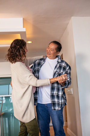 Diverse couple dancing slowly near kitchen island with bar stools at home under recessed lights....