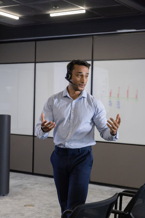 Man presenting charts on whiteboard in modern office boardroom wearing headset microphone. Business,...