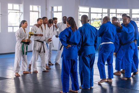 Diverse martial arts teams holding gold trophy and congratulating each other in training hall....