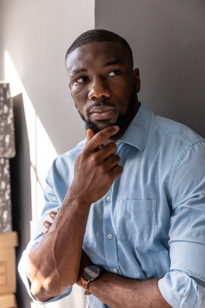 African American man standing at office, wearing shirt and checking wristwatch by cardboard boxes....