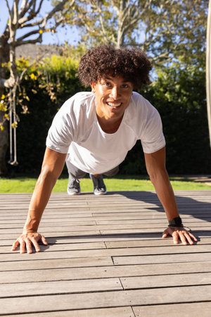 African American man performing push-ups on deck near rope swing wearing running shoes, smartwatch....