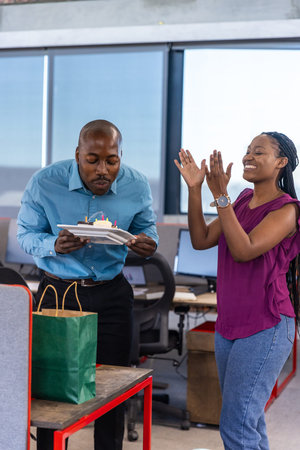 African American coworkers celebrating birthday in office holding cake plate beside gift bag. Celebration, teamwork, diversity, camaraderie, professional, vibrant, cheerfulの写真素材