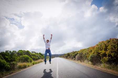 Man jumping midair on long straight road with white center line and sharp shadow. Traveler,...