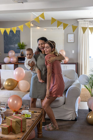 Diverse family hugging and celebrating in living room with gold pink balloons and gift boxes....