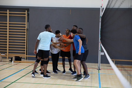 African American men in sportswear and knee pads placing hands center on hardwood court near net. Teamwork, huddle, volleyball, gym, athletic, focus, motivationの写真素材