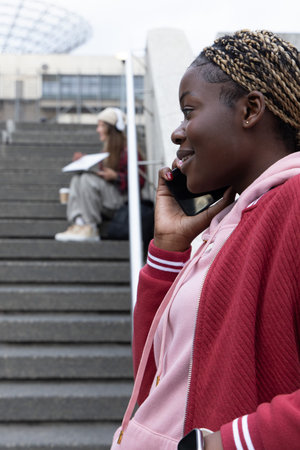 African American woman standing right of campus steps in pink hoodie talking on phone, copy space....