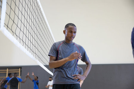 African American male teammates standing at gym near net adjusting gray shirt by wall bars. Volleyball, teamwork, court, practice, warmup, athleticwear, focusの写真素材