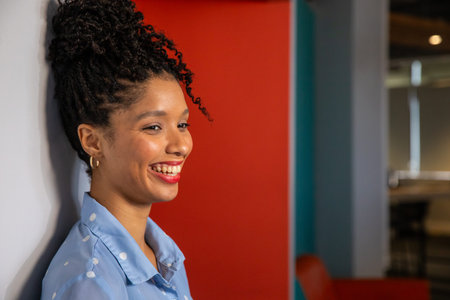 African American woman leaning against white wall, smiling, wearing blue polka shirt, copy space....