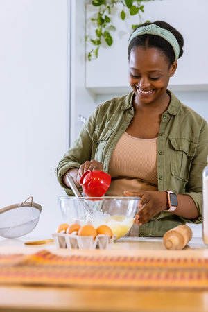 African American woman pouring from red measuring cup into mixing bowl and whisking in kitchen....