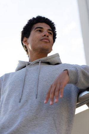 African American teenage male leaning on metal railing wearing light gray hoodie and gazing upward....