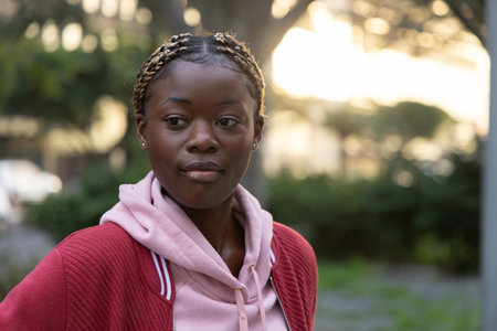 African American woman standing in park wearing pink hoodie and red jacket with braided hair....