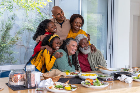 Multigenerational African American family gathering around wooden table at home salad corn bread. Wood, daylight, centerpiece, glassware, napkins, garden, warmthの写真素材
