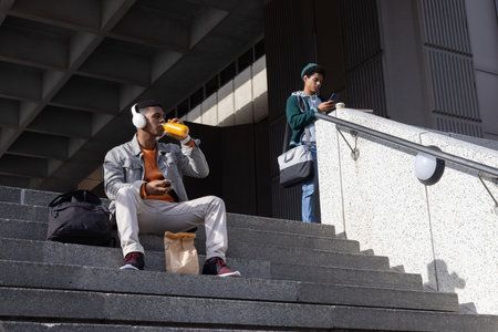 African American men on campus steps, sitting and standing, sipping from bottle, checking phones....