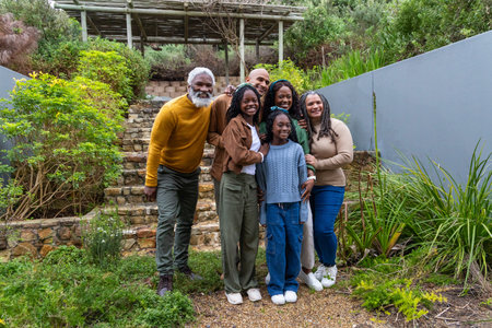 African American multigenerational family posing on gravel path by stone steps in casual clothing....