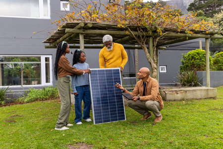 African American family senior dad, teen girls checking solar panel while tech with laptop in yard....
