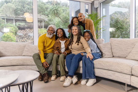 African American multi-gen family posing on sectional sofa in modern living room with large windows....