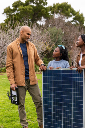 African American family holding solar panel testing inverter cord on lawn, child in blue sweater....