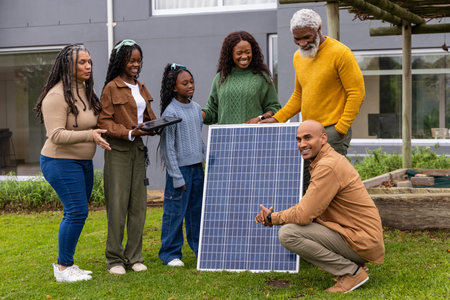 African American family with Indian tech inspecting solar panel, tablet on lawn by gray house....