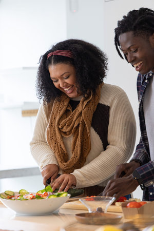 African American couple chopping greens and making salad in home kitchen near wooden cutting board. Cooking, vegetables, slicing, prep, warmth, natural, plaidの写真素材