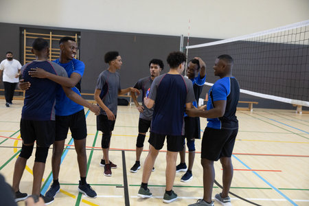 African American male team gathering on wood court near volleyball net, wearing blue-gray jerseys....