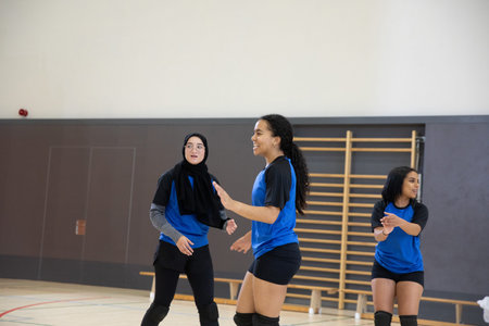 Three teenage female athletes standing on school gym court wearing blue-black jerseys and knee pads. Volleyball, team, practice, training, uniform, jersey, headscarfの写真素材