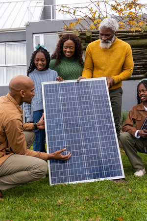 African American family gathering and holding solar panel in backyard while girl holding tablet....