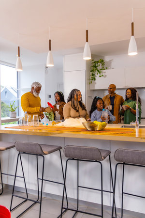 African American family gathering around wood-topped kitchen island at home, passing glass pitchers....